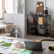 Bureau d'architecte ou urbaniste avec maquette de maison écologique, éoliennes miniatures et plans de paysage durable sur le bureau, environnement de travail moderne et lumineux