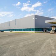 Entrepôt industriel moderne avec façade grise et grandes fenêtres bleues, parking extérieur avec véhicules